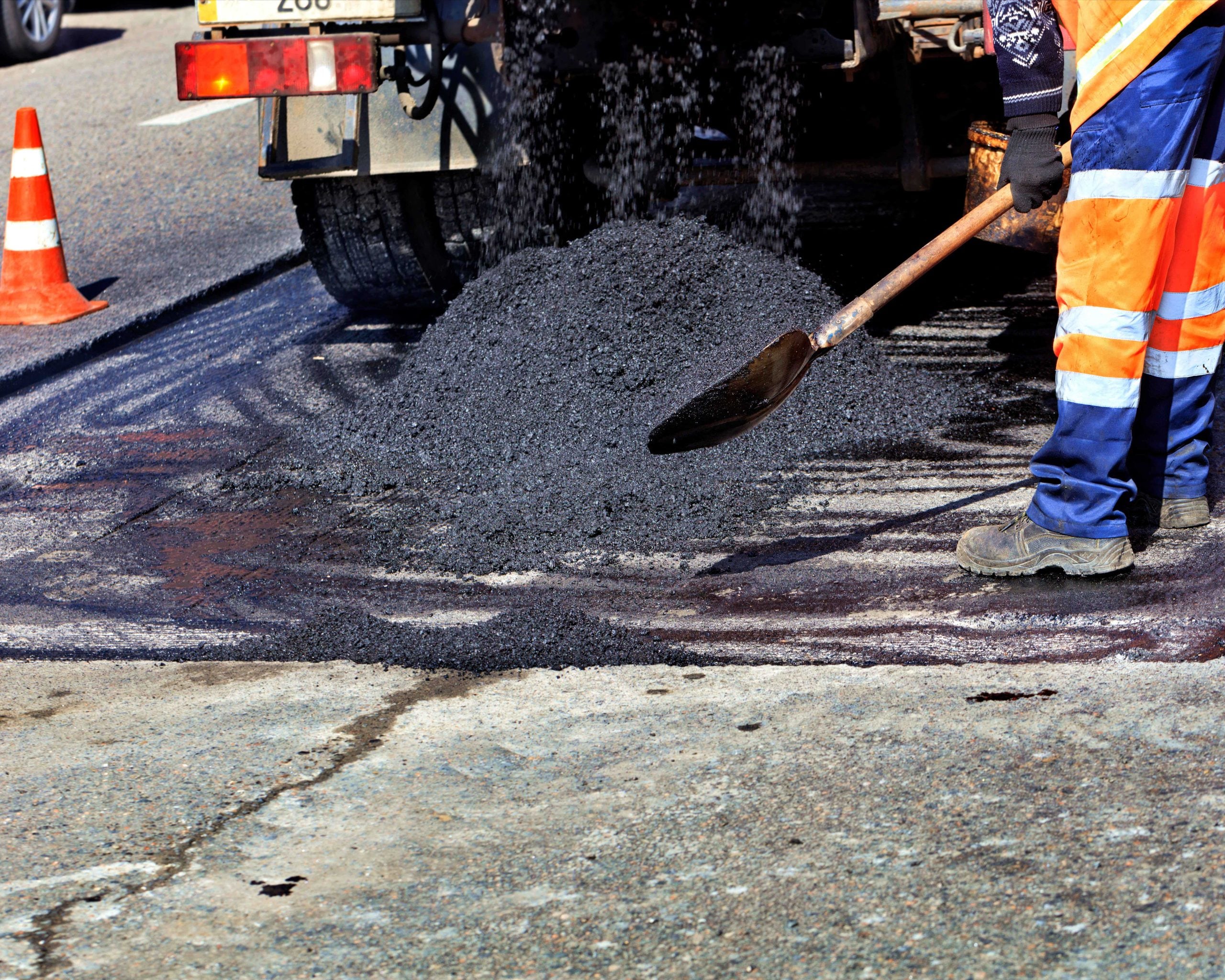 An asphalt contractor shovels asphalt as it is poured out of a truck.